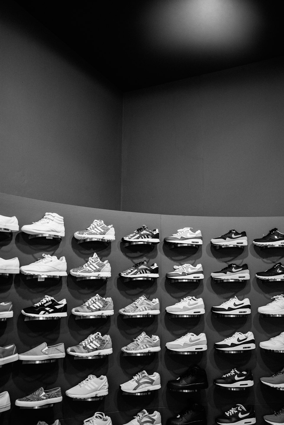 Zapatillas deportivas expuestas en estanterías contra una pared gris.