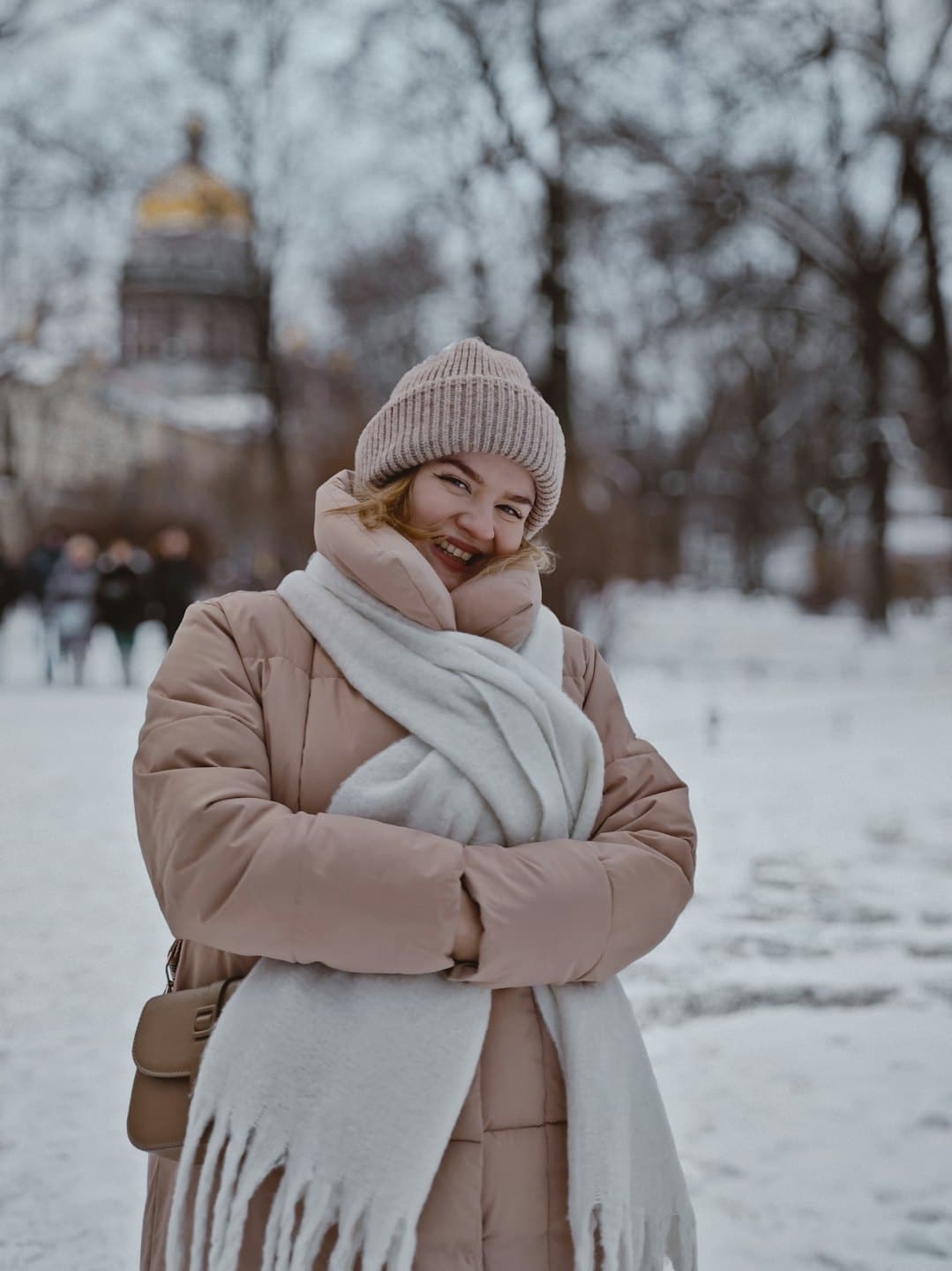 Mujer con abrigo beige acolchado de pie en la nieve.