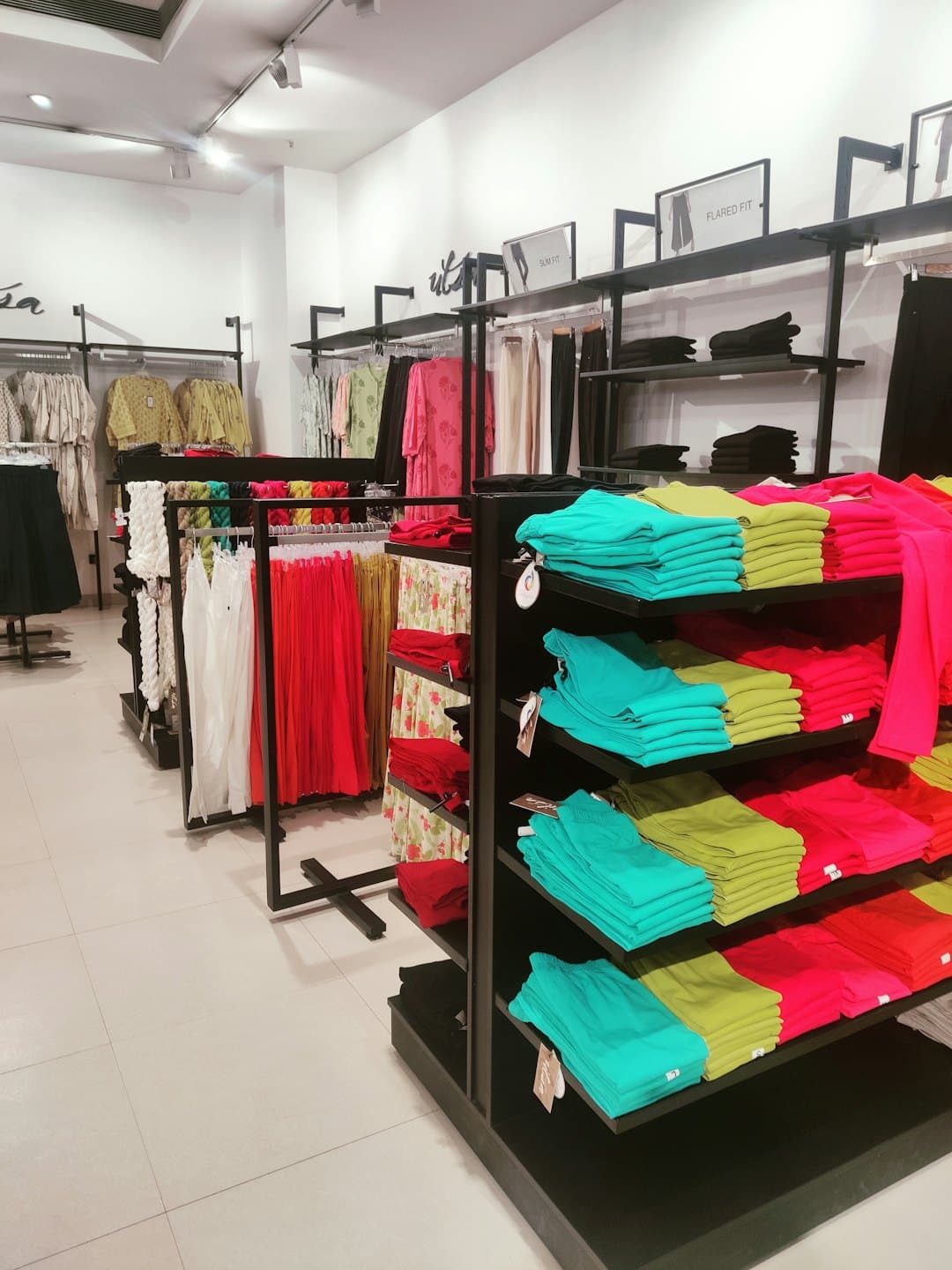 Una tienda de ropa moderna muestra percheros con ropa colorida doblada y colgada.