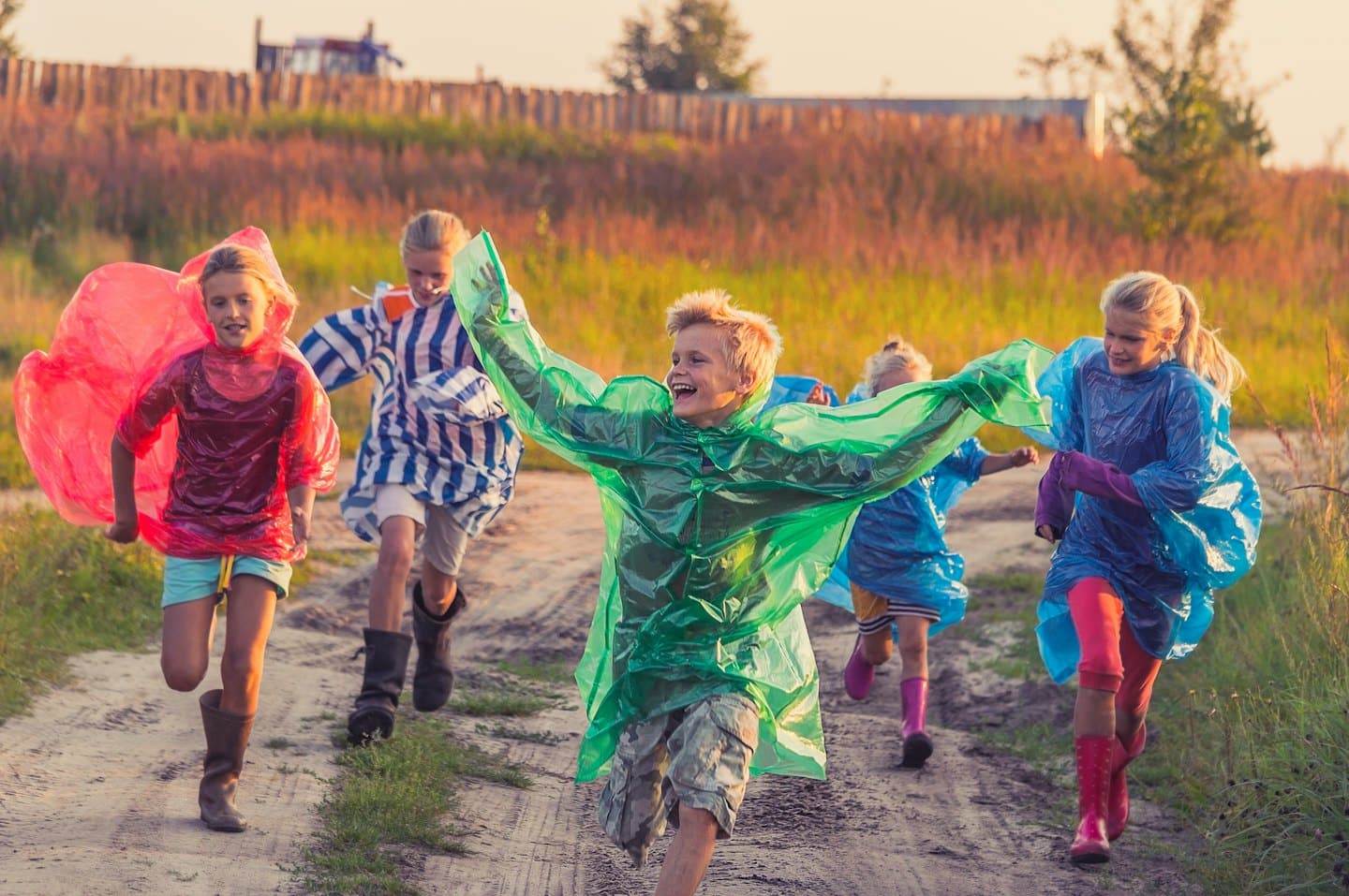 Niños con ponchos de lluvia de colores corren por un camino de hierba.